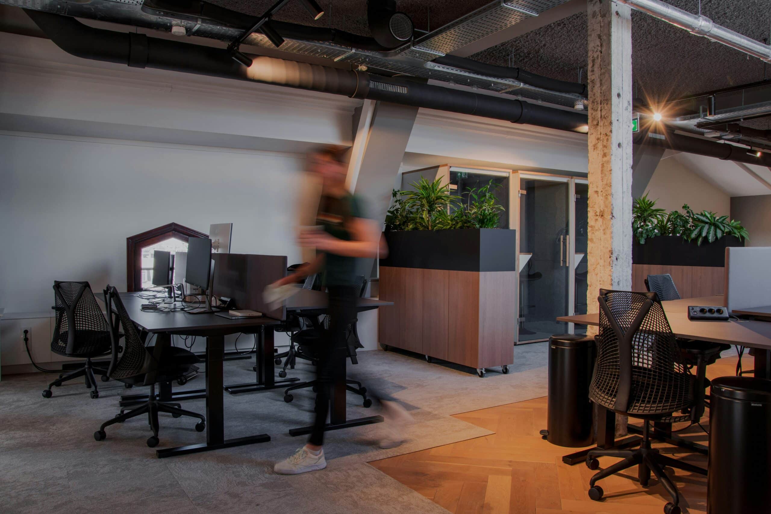 Ein modernes Büro mit PC Ausstattung, Pflanzen und einem modernen Design. In der Mitte ist ein Mann, der verschwommen ist und im Büro läuft